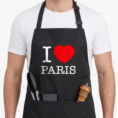 Tablier de cuisine noir avec le logo I Love Paris en blanc et un grand cœur rouge au centre du design imprimé.