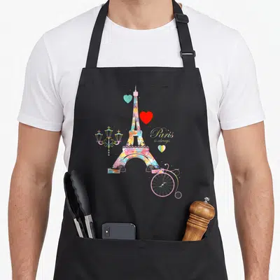 Tablier de cuisine noir avec une illustration colorée de la Tour Eiffel, des cœurs et un vélo rose stylisé sur fond uni.