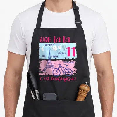 Tablier de cuisine noir avec illustration colorée de la Tour Eiffel, d'un vélo et du texte Ooh La La C'est Magnifique.