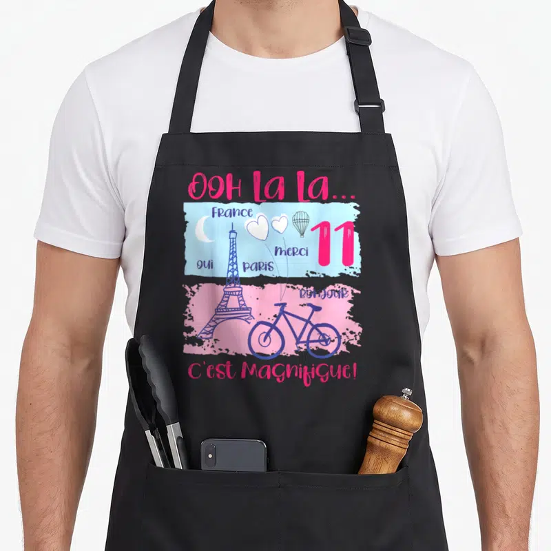 Tablier de cuisine noir avec illustration colorée de la Tour Eiffel, d'un vélo et du texte Ooh La La C'est Magnifique.