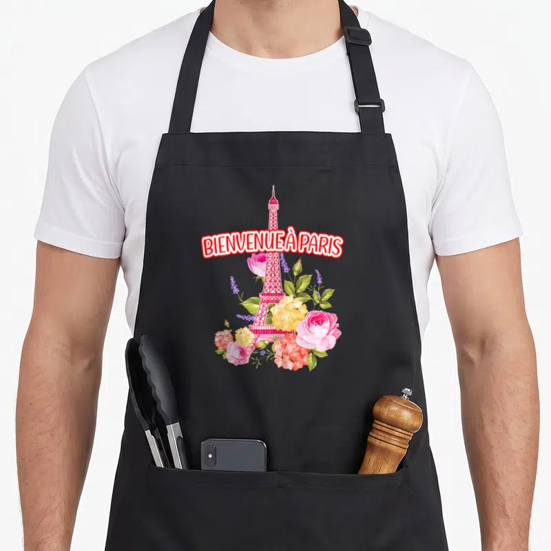 Tablier de cuisine noir avec une tour Eiffel rose et des fleurs multicolores sur le devant.