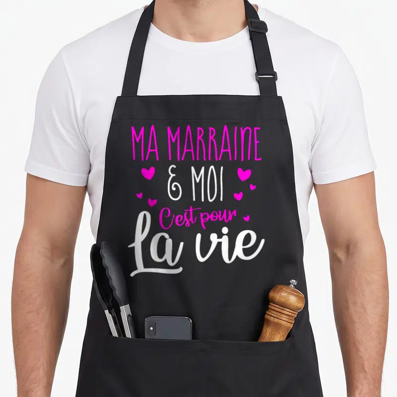 Tablier de cuisine noir avec inscription Ma marraine et moi c'est pour la vie en rose et blanc entouré de petits coeurs.