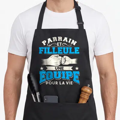 Tablier de cuisine noir avec inscription Parrain et Filleule Une Équipe Pour La Vie et illustration de deux poings s'affrontant amicalement.