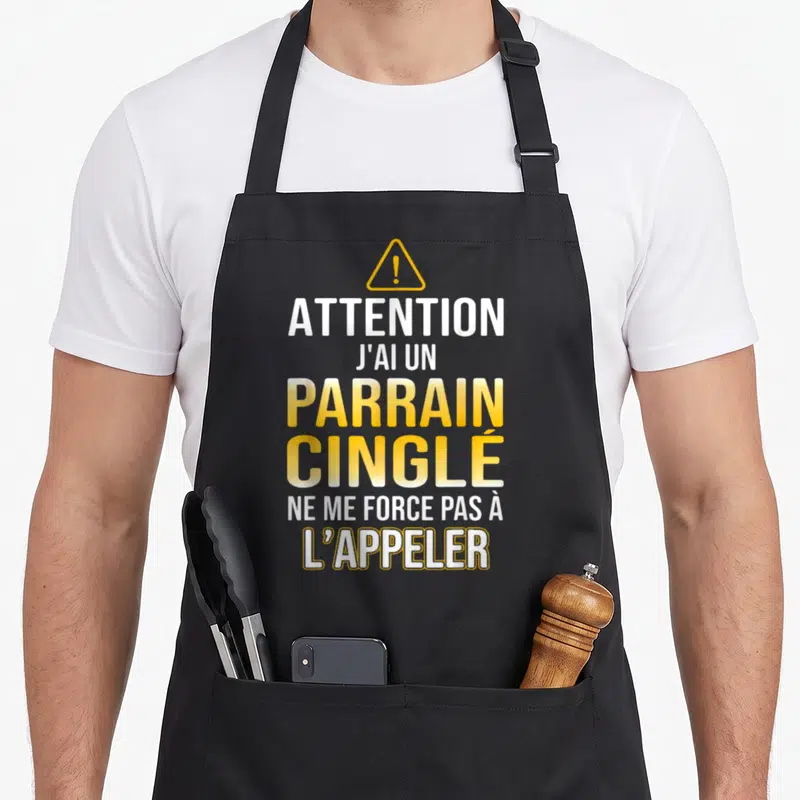 Tablier de cuisine noir avec message jaune et blanc Attention j'ai un parrain cinglé ne me force pas à l'appeler sous un triangle de signalisation.