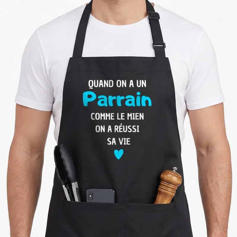 Tablier de cuisine noir avec inscription blanche et bleue quand on a un parrain comme le mien sur fond uni.