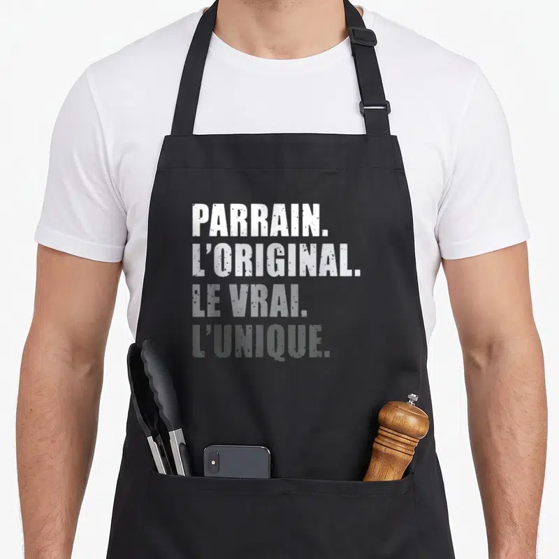 Tablier de cuisine noir avec le texte blanc et gris « Parrain. L'original. Le vrai. L'unique. » imprimé au centre.