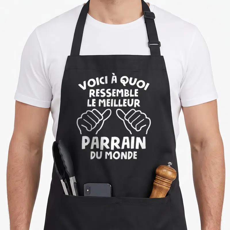 Tablier de cuisine noir avec inscription Voici à quoi ressemble le meilleur parrain du monde et deux mains faisant des pouces levés.