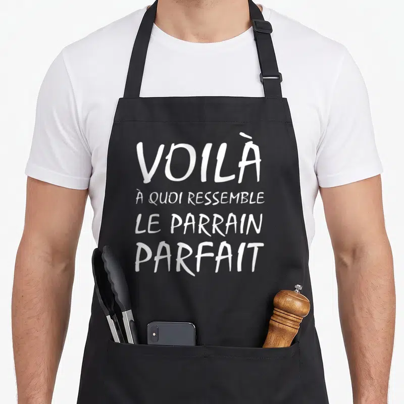 Tablier de cuisine noir avec le texte blanc « Voilà à quoi ressemble le parrain parfait » imprimé au centre du torse.