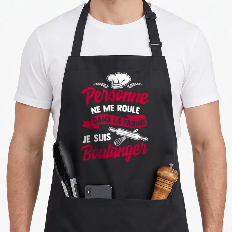 Tablier de cuisine noir avec inscription Personne ne me roule dans la farine et ustensiles de boulangerie en rose et blanc.