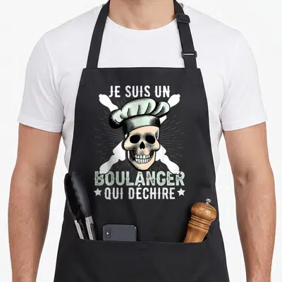 Tablier de cuisine noir avec un crâne portant une toque de chef et des os croisés en arrière-plan.