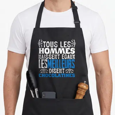 Tablier de cuisine noir avec le texte humoristique Tous les hommes naissent égaux les meilleurs disent chocolatines en blanc et bleu.