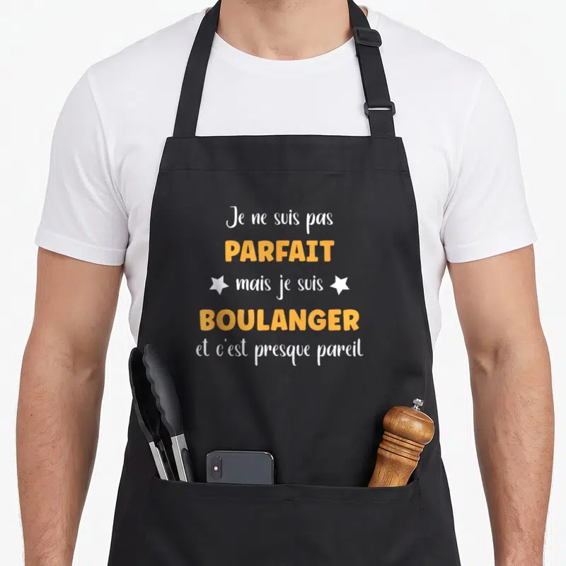 Tablier de cuisine noir avec le texte Je ne suis pas parfait mais je suis boulanger en orange et blanc orné d'étoiles.