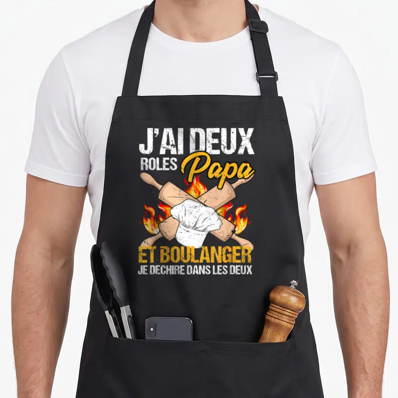 Tablier de cuisine noir avec deux rouleaux à pâtisserie croisés, un chapeau de chef et des flammes stylisées en arrière-plan.