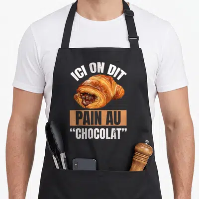 Tablier de cuisine noir avec illustration colorée d'un pain au chocolat et texte blanc humoristique.