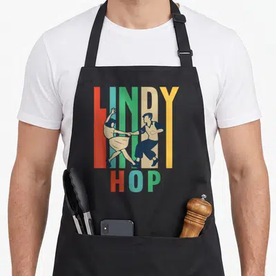 Tablier de cuisine noir avec illustration vintage d'un couple dansant le Lindy Hop sur des lettres colorées.