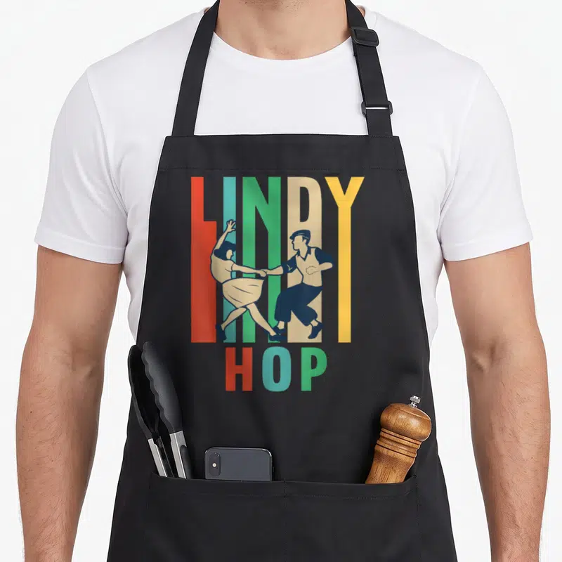 Tablier de cuisine noir avec illustration vintage d'un couple dansant le Lindy Hop sur des lettres colorées.