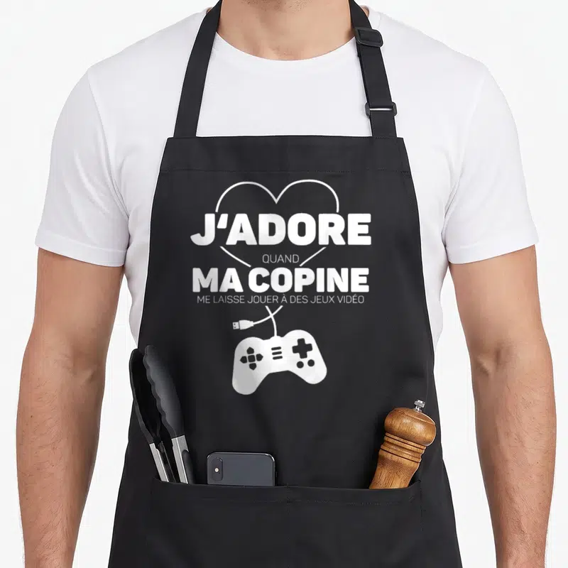 Tablier de cuisine noir avec inscription blanche J'adore quand ma copine et une illustration de manette de jeu vidéo.