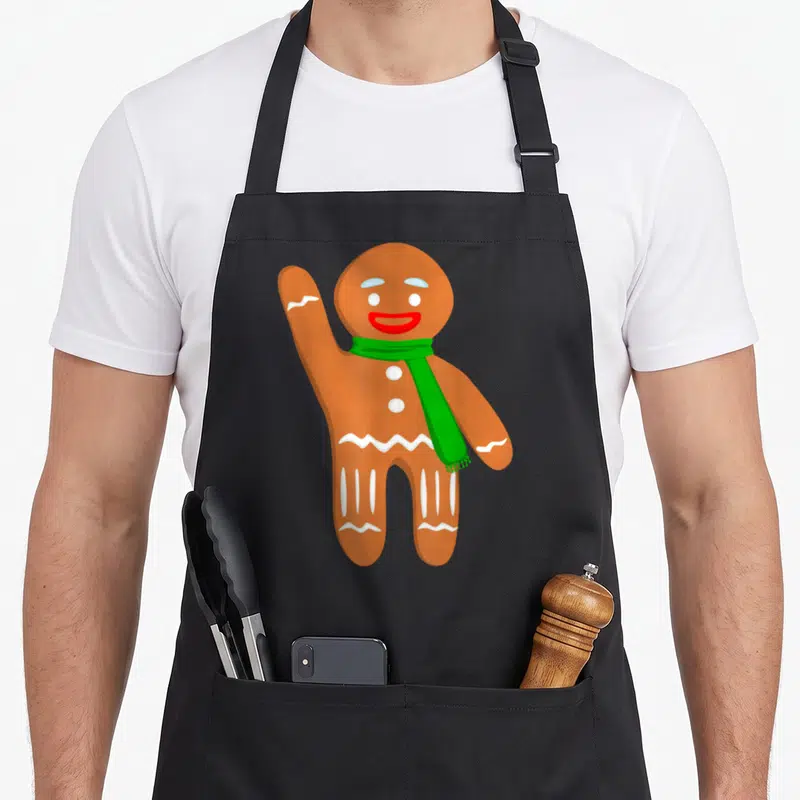 Tablier de cuisine noir avec illustration d'un bonhomme en pain d'épice souriant et une écharpe verte.