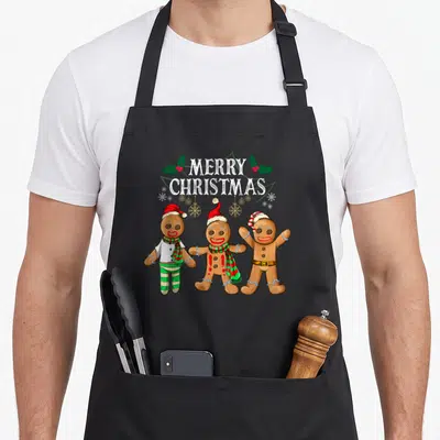Tablier de cuisine noir avec trois bonhommes en pain d'épice et l'inscription Merry Christmas sur le devant.