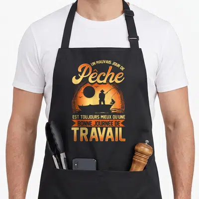 Tablier de cuisine noir avec silhouette de pêcheur au soleil et texte humoristique sur la pêche et le travail.