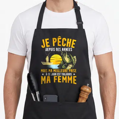 Tablier de cuisine noir avec silhouette de pêcheur, soleil jaune et gros poisson vert sautant de l'eau.