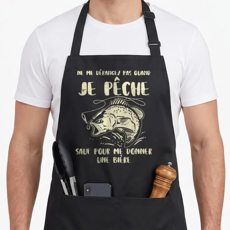 Tablier de cuisine noir avec illustration de poisson sautant et texte humoristique sur la pêche et la bière.