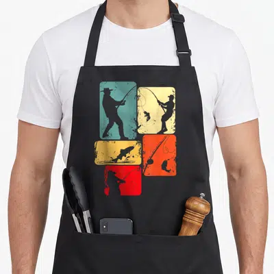 Tablier de cuisine noir avec cinq rectangles colorés montrant des silhouettes de pêcheurs et un poisson qui saute.