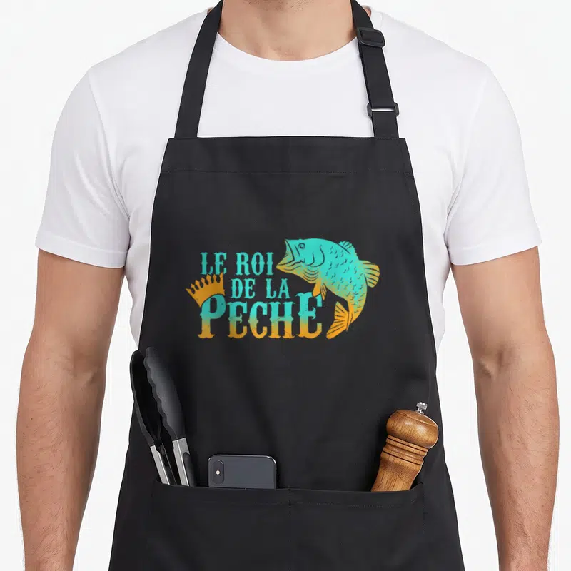 Tablier de cuisine noir avec illustration d'un poisson sautant turquoise et orange et le texte Le Roi de la Pêche.