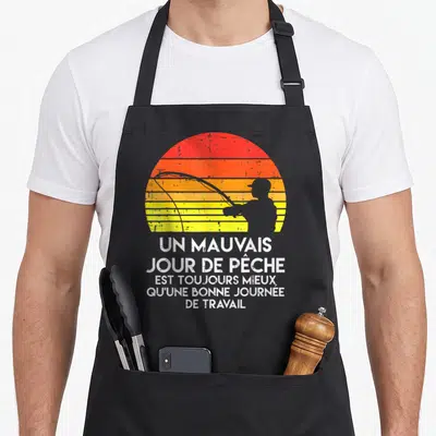Tablier de cuisine noir avec silhouette de pêcheur et texte blanc sur fond de soleil rayé orange et jaune.