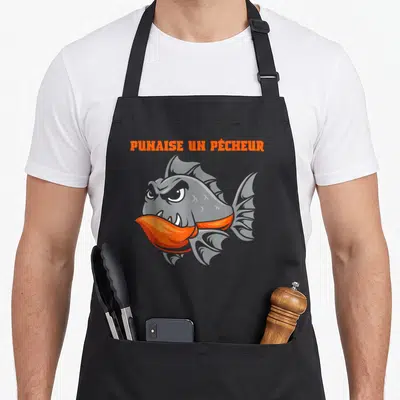 Tablier de cuisine noir avec illustration d'un poisson orange et gris aux dents acérées et texte « Punaise un Pêcheur » en haut.
