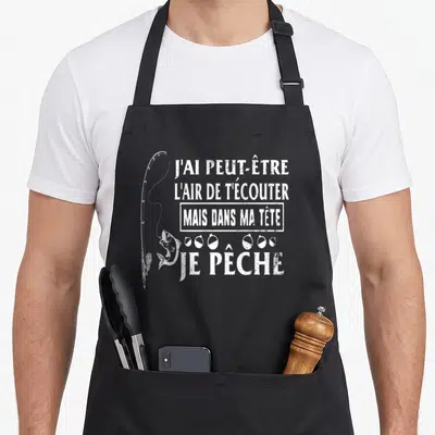 Tablier de cuisine noir avec une illustration de canne à pêche et le texte J'ai peut-être l'air de t'écouter mais dans ma tête je pêche en blanc.