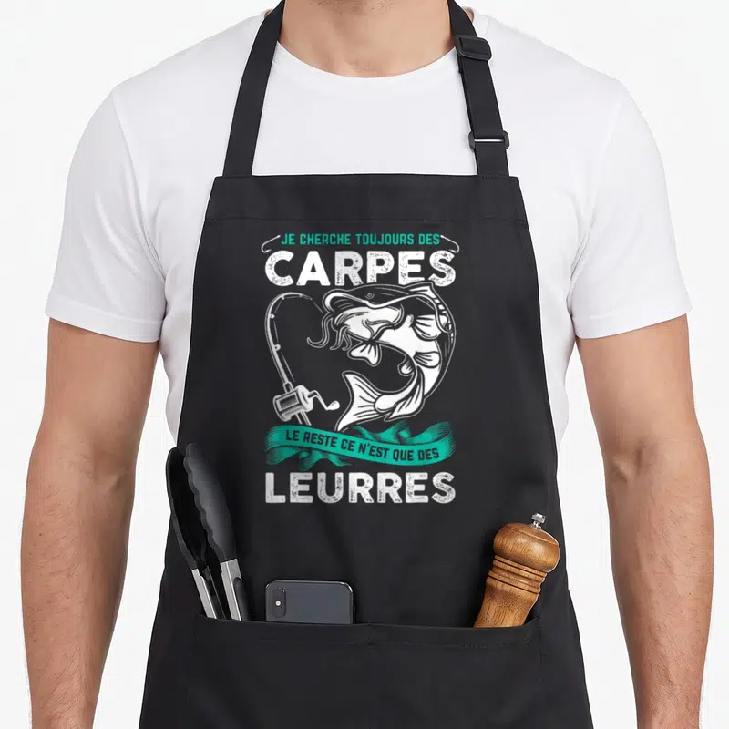 Tablier de cuisine noir avec illustration blanche d'une carpe, canne à pêche et texte humoristique sur le thème de la pêche.
