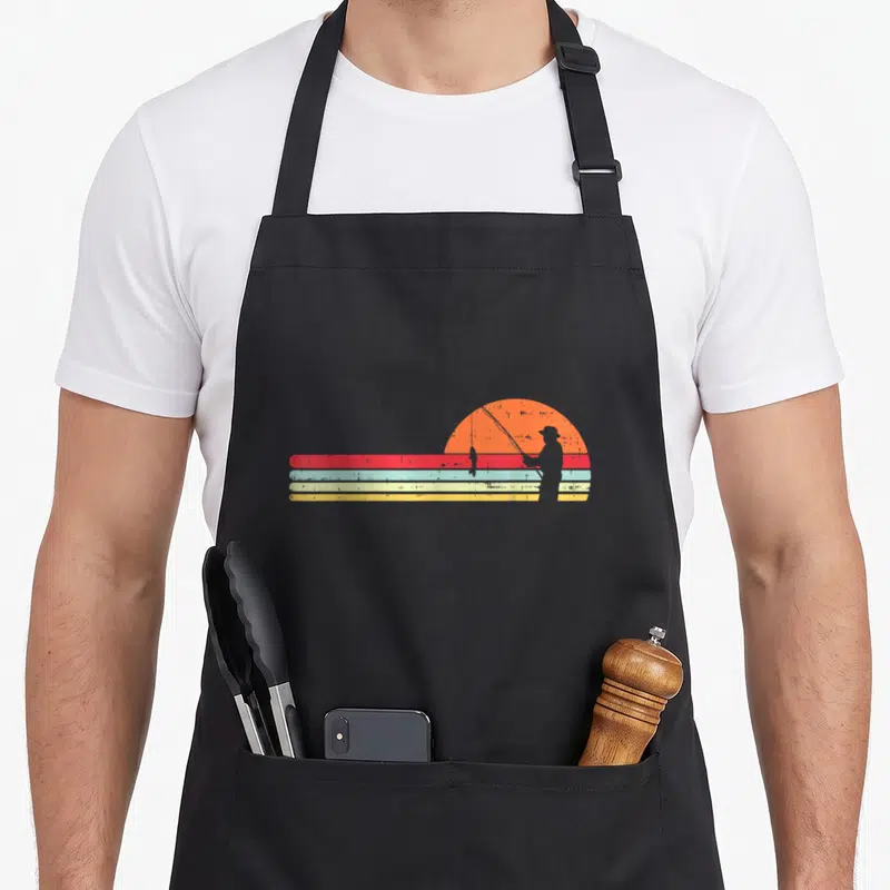 Tablier de cuisine noir avec silhouette de pêcheur devant un soleil orange et des bandes colorées style vintage.