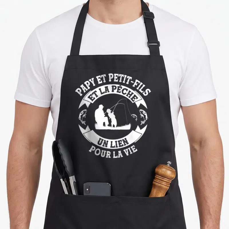 Tablier de cuisine noir avec un motif circulaire blanc représentant un grand-père et un enfant en silhouette au bord de l'eau.