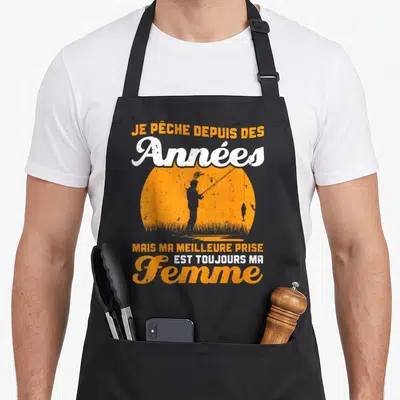 Tablier de cuisine noir avec silhouette orange d'un pêcheur et texte humoristique sur la femme comme meilleure prise.