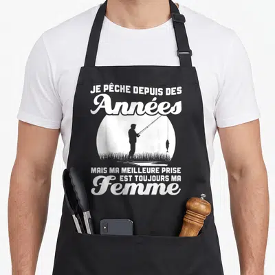 Tablier de cuisine noir avec silhouette blanche d'un pêcheur et texte Je pêche depuis des années ma femme