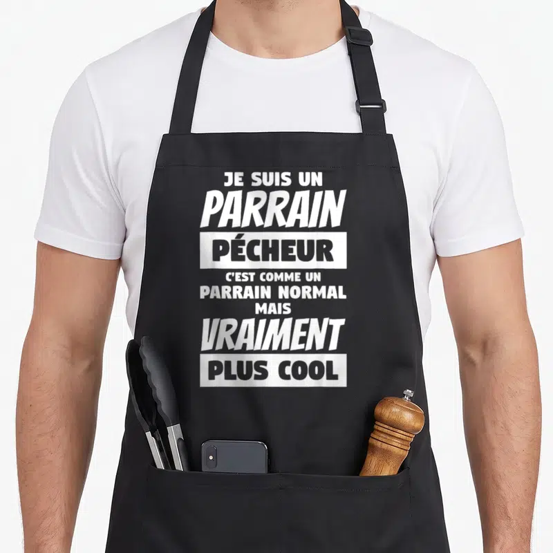 Tablier de cuisine noir avec le texte blanc Je suis un parrain pêcheur vraiment plus cool imprimé au centre du vêtement.