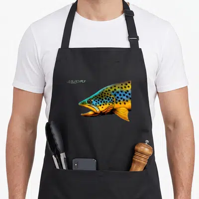 Tablier de cuisine noir avec tête de truite marron aux teintes bleues et oranges, logo Black Fly Fishing en haut à gauche.