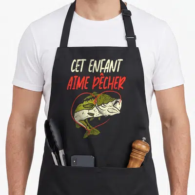 Tablier de cuisine noir avec illustration d'un poisson vert dans un cœur rouge et le texte Cet Enfant Aime Pêcher en haut.