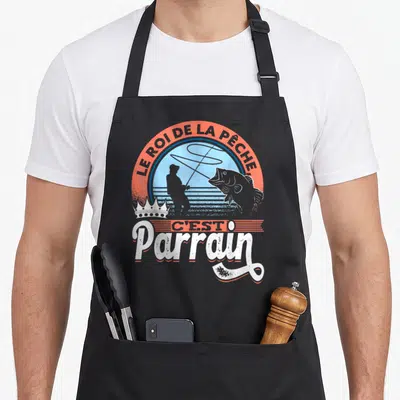 Tablier de cuisine noir avec illustration d'un pêcheur, une crown et le texte Le roi de la pêche c'est parrain en orange et blanc.
