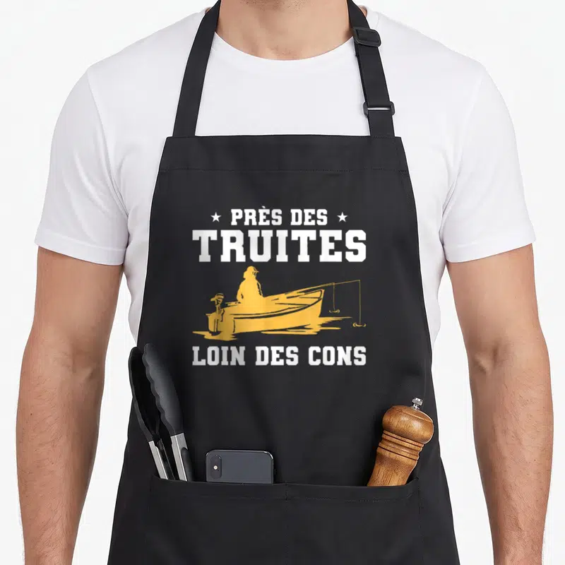 Tablier de cuisine noir avec silhouette pêcheur en barque jaune et texte blanc Près de truites loin des cons