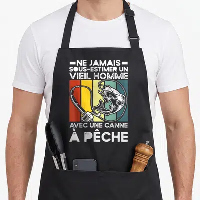 Tablier de cuisine noir avec illustration vintage d'une canne à pêche, d'un poisson sautant et texte blanc sur fond de bandes colorées.
