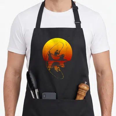 Tablier de cuisine noir avec illustration d'un pêcheur en barque devant un soleil orange et son reflet dans l'eau.