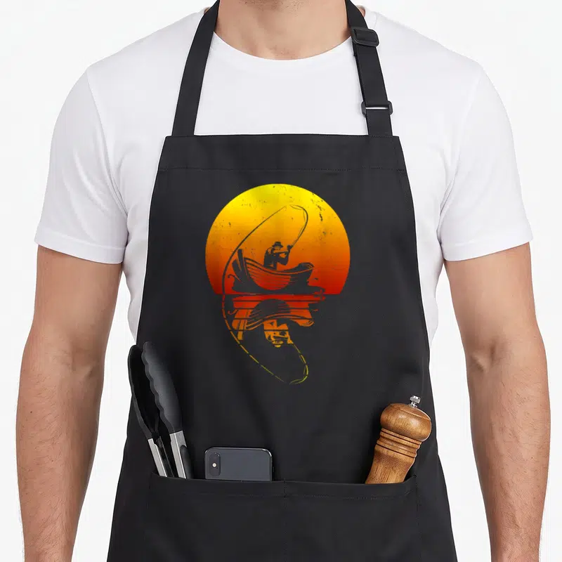 Tablier de cuisine noir avec illustration d'un pêcheur en barque devant un soleil orange et son reflet dans l'eau.