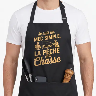 Tablier de cuisine noir avec inscription dorée Je suis un mec simple j'aime la pêche et la chasse et deux illustrations de pêcheurs.