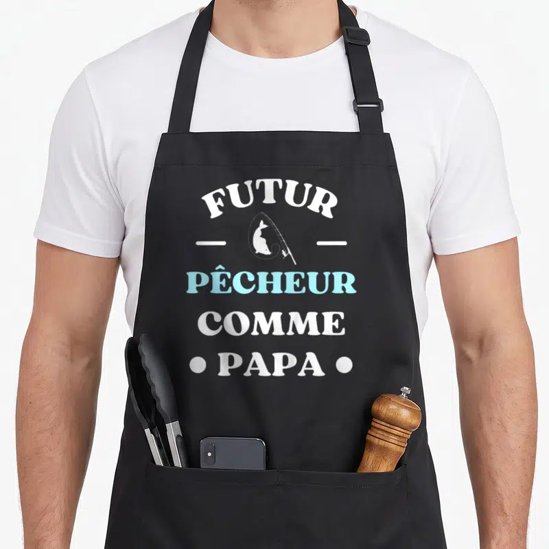 Tablier de cuisine noir avec inscription Futur pêcheur comme papa et silhouette de poisson sur canne à pêche en bleu clair.
