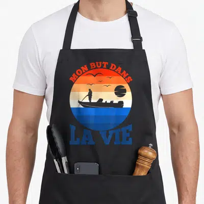 Tablier de cuisine noir avec illustration circulaire d'un pêcheur en bateau et texte Mon but dans la vie en orange et bleu.