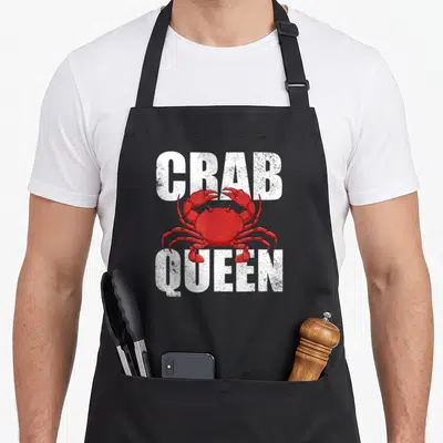 Tablier de cuisine noir avec un crabe rouge et le texte CRAB QUEEN en lettres blanches délavées.