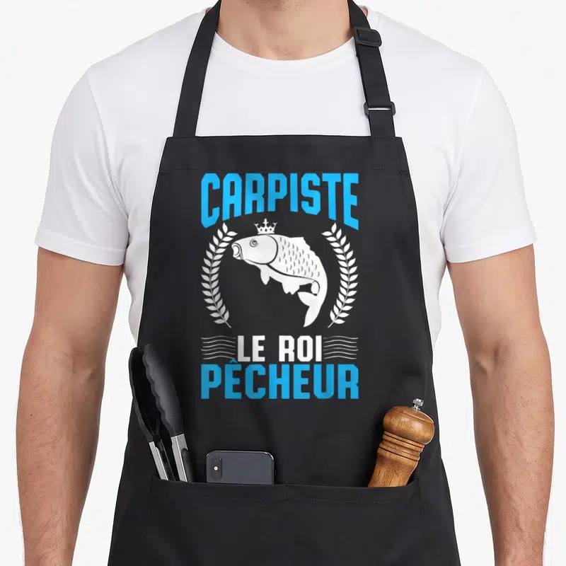 Tablier de cuisine noir avec une carpe blanche couronnée encadrée de lauriers et le texte Carpiste Le Roi Pêcheur en bleu et blanc.