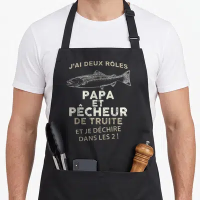 Tablier de cuisine noir avec illustration de truite et texte J'ai deux rôles Papa et Pêcheur de truite en typographie texturée.